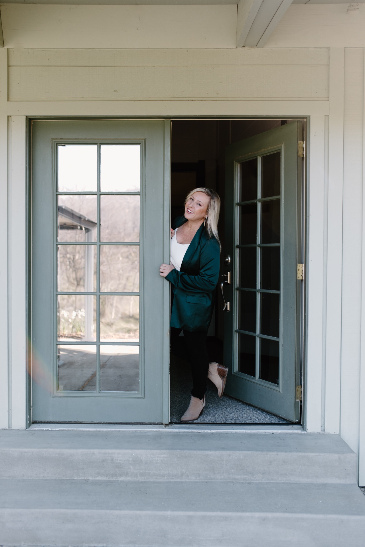 Cassie stepping through sage-green French doors